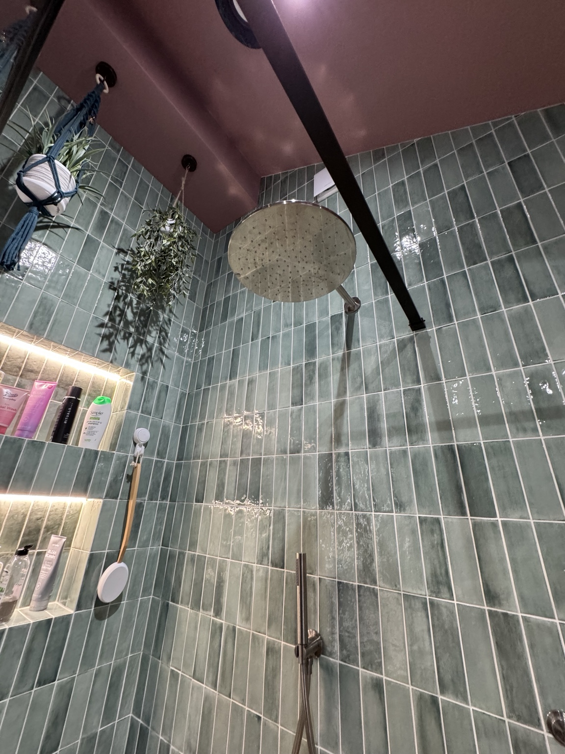 Rainfall shower and lit niches in a green tiled bathroom