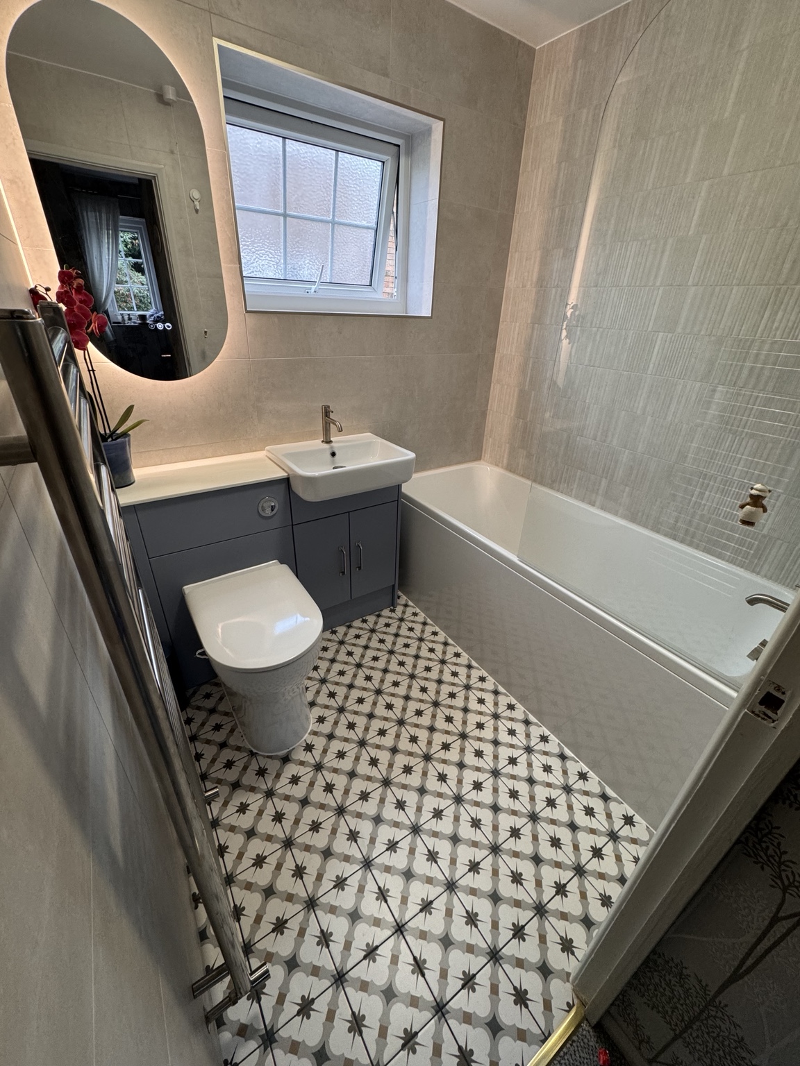 Bathroom with patterned floor tiles, bath and illuminated mirror