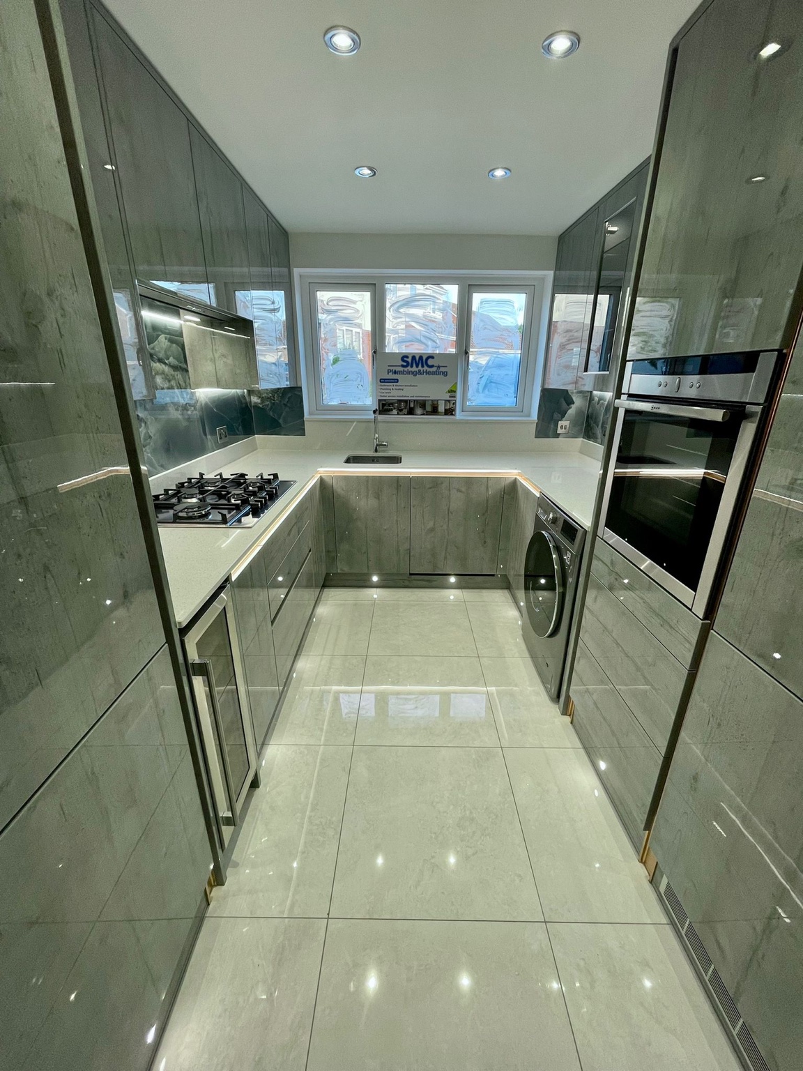Kitchen after the refit, with gloss cabinets, light tiled flooring, fitted appliances and feature lighting