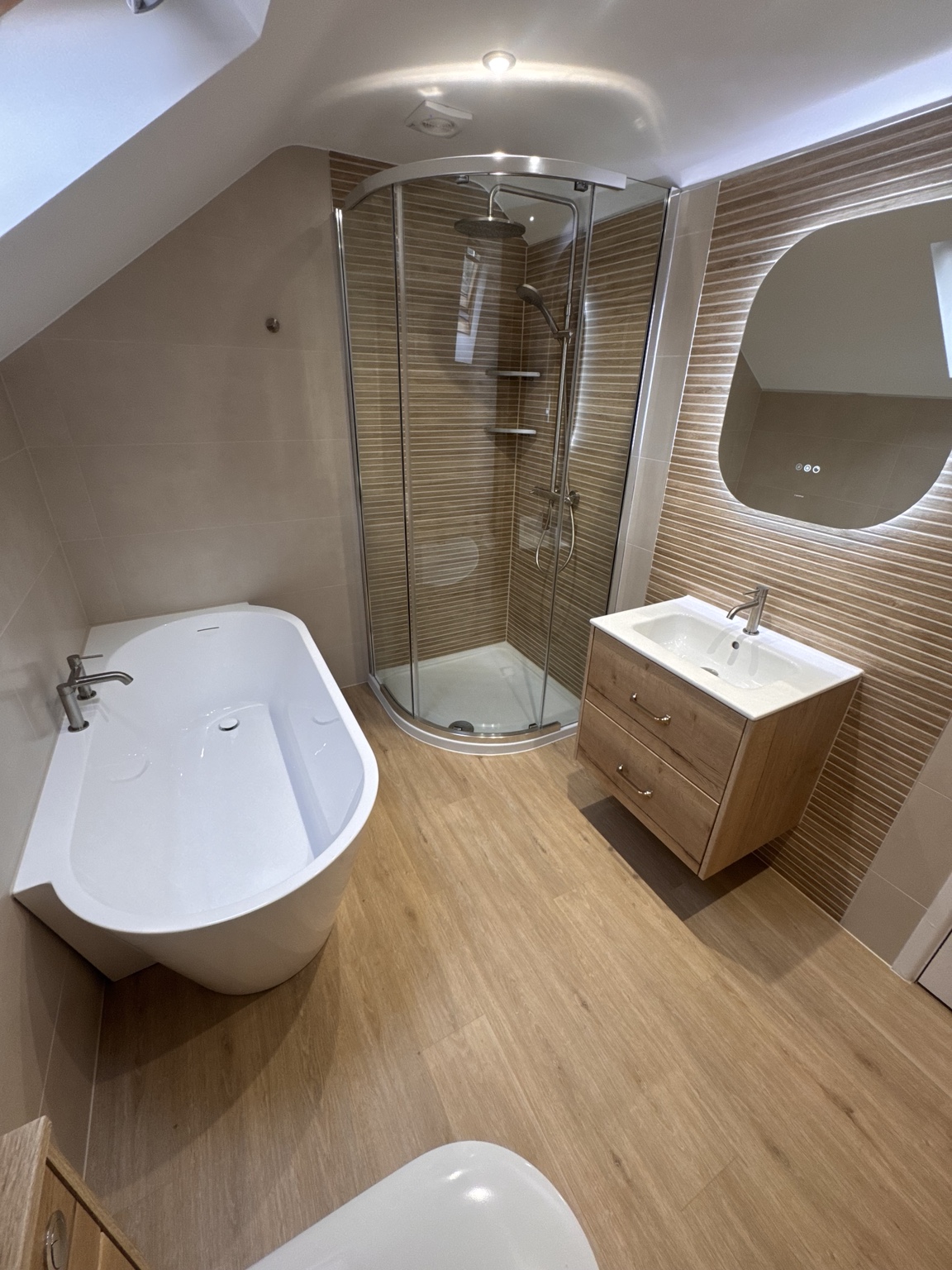 The same loft bathroom after renovation, with a freestanding bath, corner shower and fitted vanity