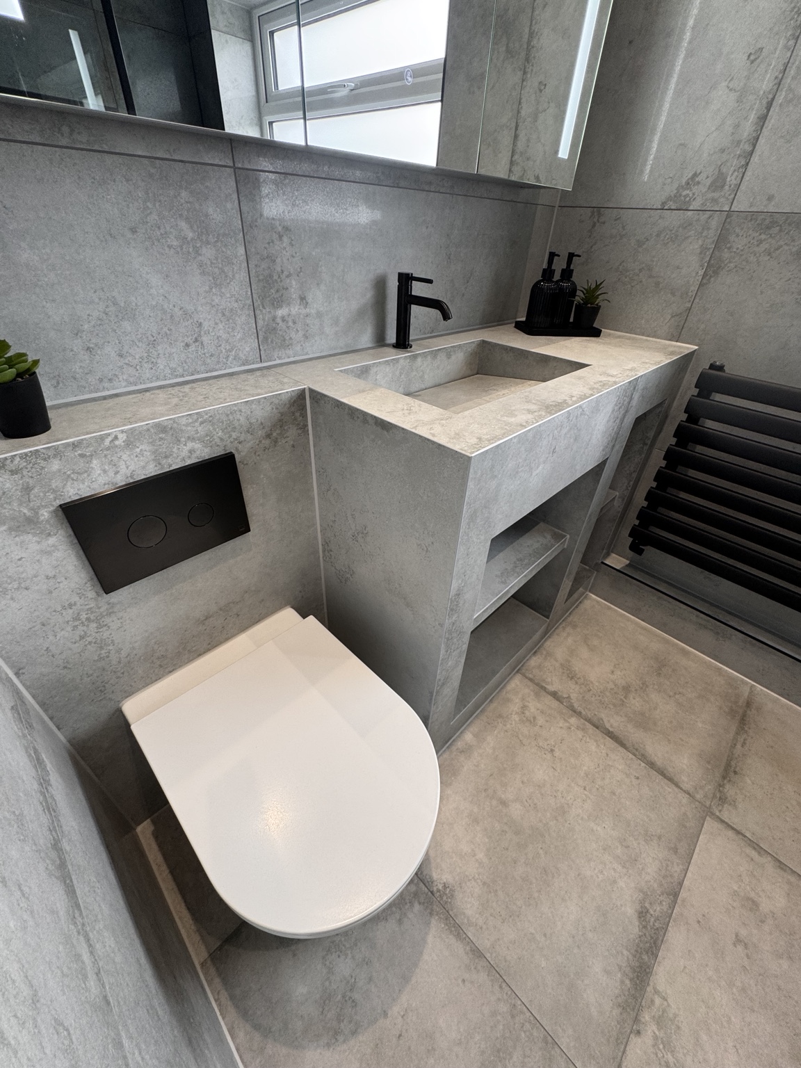 Wall-hung toilet beside the tiled basin and concealed flush plate